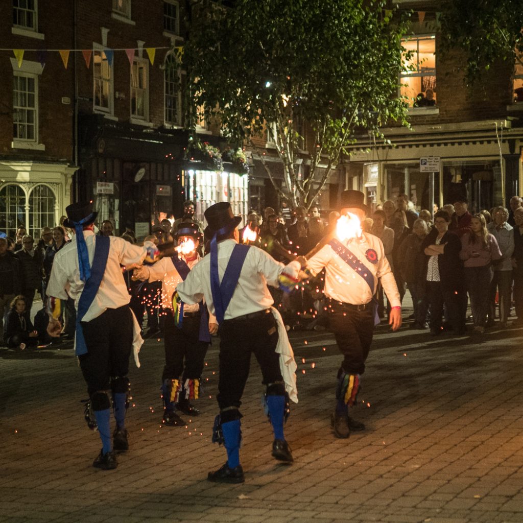 Four morris dancers clash sticks. The sticks are on fire and the dance is happening at night.